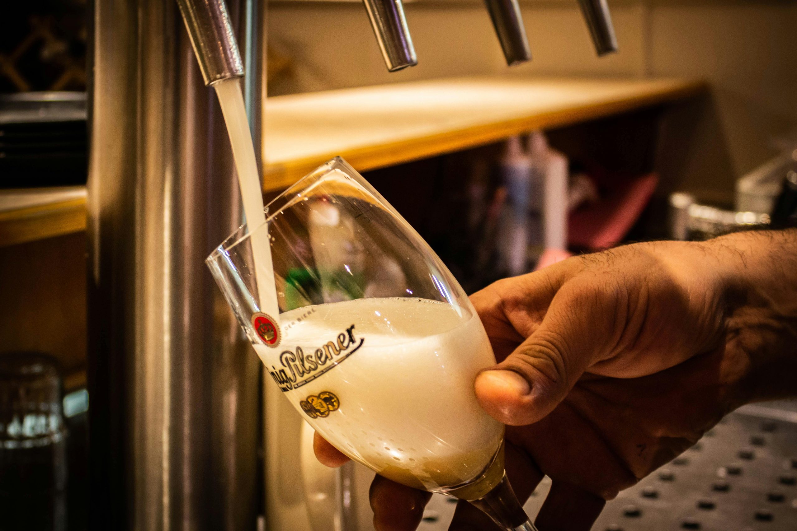 A hand pouring a fresh beer from a tap into a glass at a bar counter.