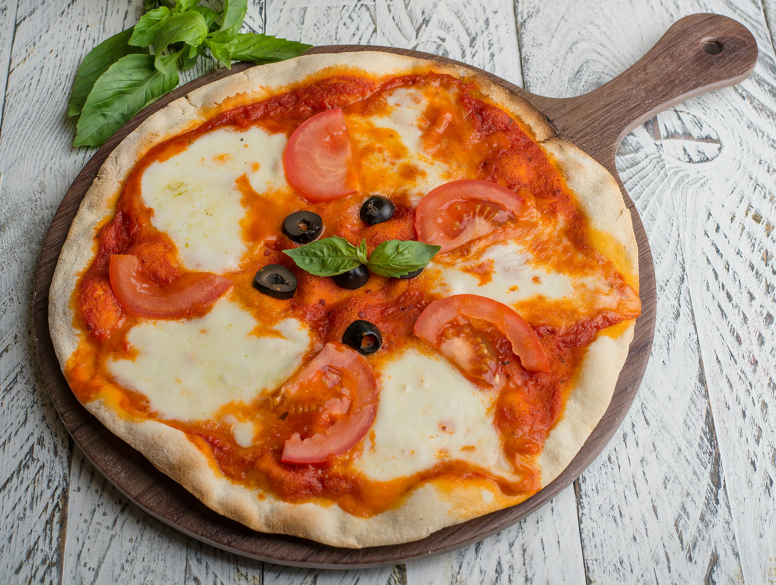 Appetizing Margherita pizza with tomatoes, olives, and fresh basil on a wooden board.