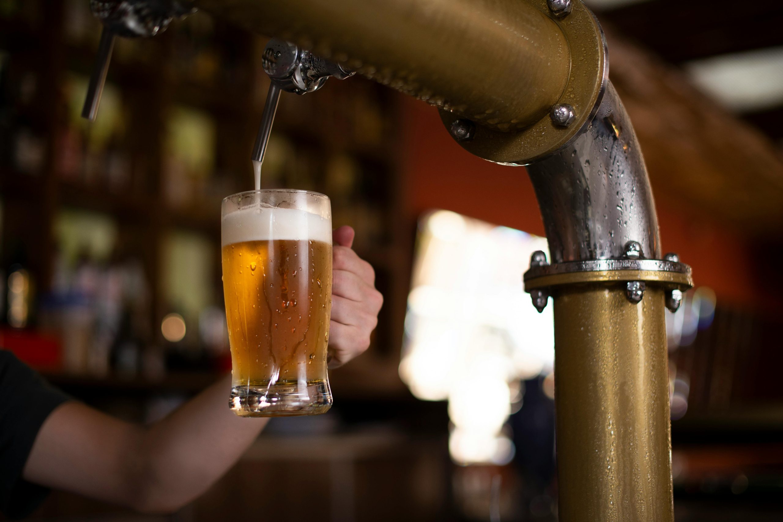 A close-up of a hand holding a mug as beer is poured from a brewery tap.