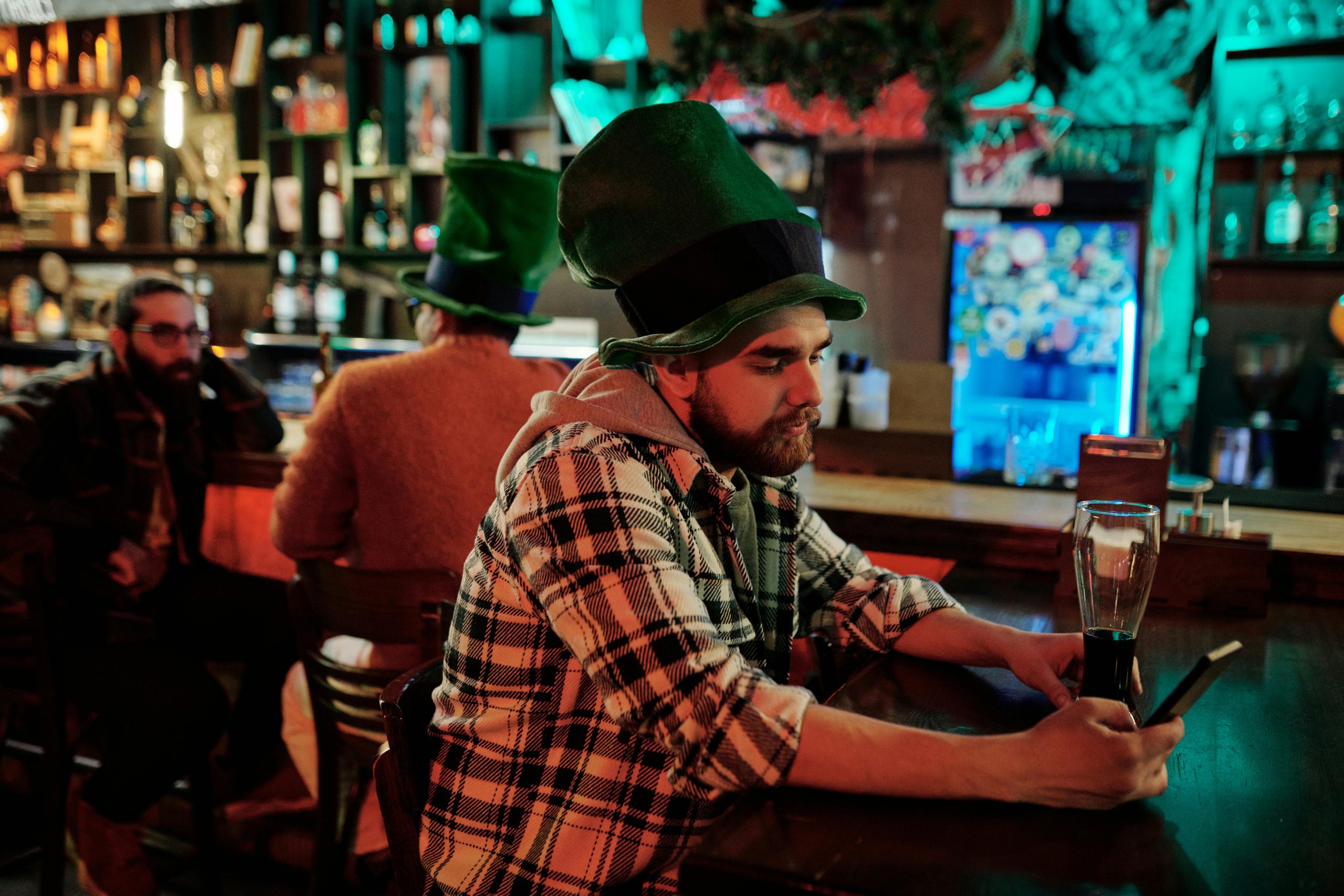 Men in green hats enjoying Saint Patrick's Day at a lively bar counter.